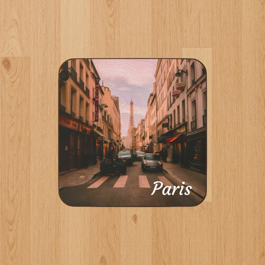Square hardboard coaster featuring a digital watercolor of a Parisian boulevard looking toward the Eiffel Tower, with warm golden building facades, pedestrians, and soft evening cobblestone light, displayed on a light wood grain surface. Part of The Painted Passport Original Series.